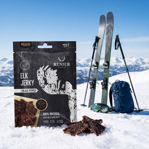 Renjer Elg Jerky med Svart Pepper i snøen ved siden av turski og staver på en solrik vinterdag i fjellet, AI-generert bilde