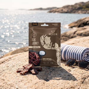 Renjer Elg Jerky med Sjøsalt på et svaberg ved sjøen, med håndkle og solbriller, AI-generert bilde