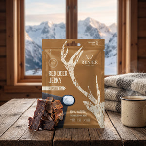Renjer Hjort Jerky med Sjøsalt på et trebord i en hytte, med ullpledd, emaljekopp og snødekte fjell utenfor vinduet, AI-generert bilde