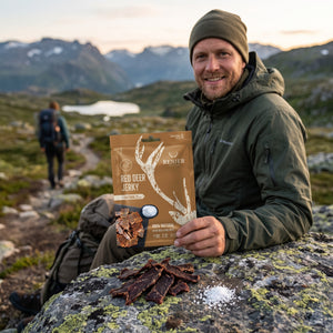 Turgåer tar en pause på fjellet og holder Renjer Hjort Jerky med Sjøsalt, AI-generert bilde