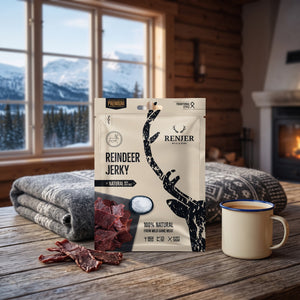 Renjer Reinsdyr Jerky med Sjøsalt på et trebord i en hytte, med ullpledd, emaljekopp og snødekte fjell utenfor vinduet, AI-generert bilde