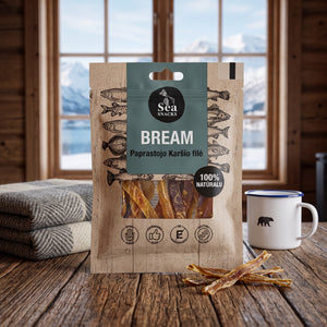 Sea Snacks tørket brasme på et trebord i en hytte, med ullpledd, emaljekopp og snødekte fjell utenfor vinduet, AI-generert bilde