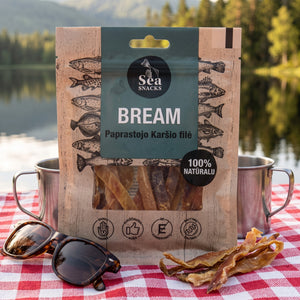 Sea Snacks tørket brasme på et rutete piknikteppe ved et skogsvann en sommerdag, med stålkopp og solbriller, AI-generert bilde