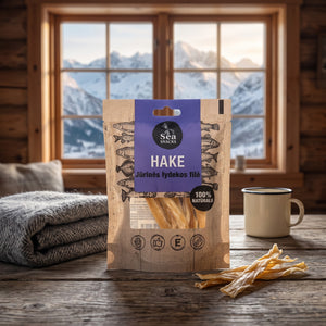 Sea Snacks tørket lysing på et trebord i en hytte, med ullpledd, emaljekopp og snødekte fjell utenfor vinduet, AI-generert bilde