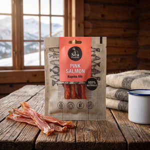 Sea Snacks tørket laks på et trebord i en hytte, med ullpledd, emaljekopp og snødekte fjell utenfor vinduet, AI-generert bilde
