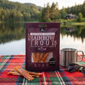 Sea Snacks tørket filet av regnbueørret på et rutete piknikteppe ved et skogsvann en sommerdag, med stålkopp og solbriller, AI-generert bilde