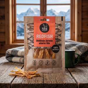 Sea Snacks tørket rødfisk fra Nord-Atlanteren på et trebord i en hytte, med ullpledd, emaljekopp og snødekte fjell utenfor vinduet, AI-generert bilde