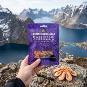 Hånd som holder Sea Snacks tørket reker fra Grønland foran et fjordlandskap, AI-generert bilde