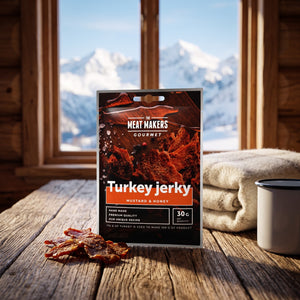 Meat Makers Gourmet Kalkun med Sennep & Honning på et trebord i en hytte, med ullpledd, emaljekopp og snødekte fjell utenfor vinduet, AI-generert bilde