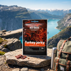 Meat Makers Gourmet Kalkun med Sennep & Honning på en stein ved en fjellsti høyt over fjorden, med ryggsekk og termos, AI-generert bilde
