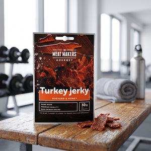 Meat Makers Gourmet Kalkun med Sennep & Honning på en benk på treningssenteret, med manualer, håndkle og drikkeflaske i bakgrunnen, AI-generert bilde